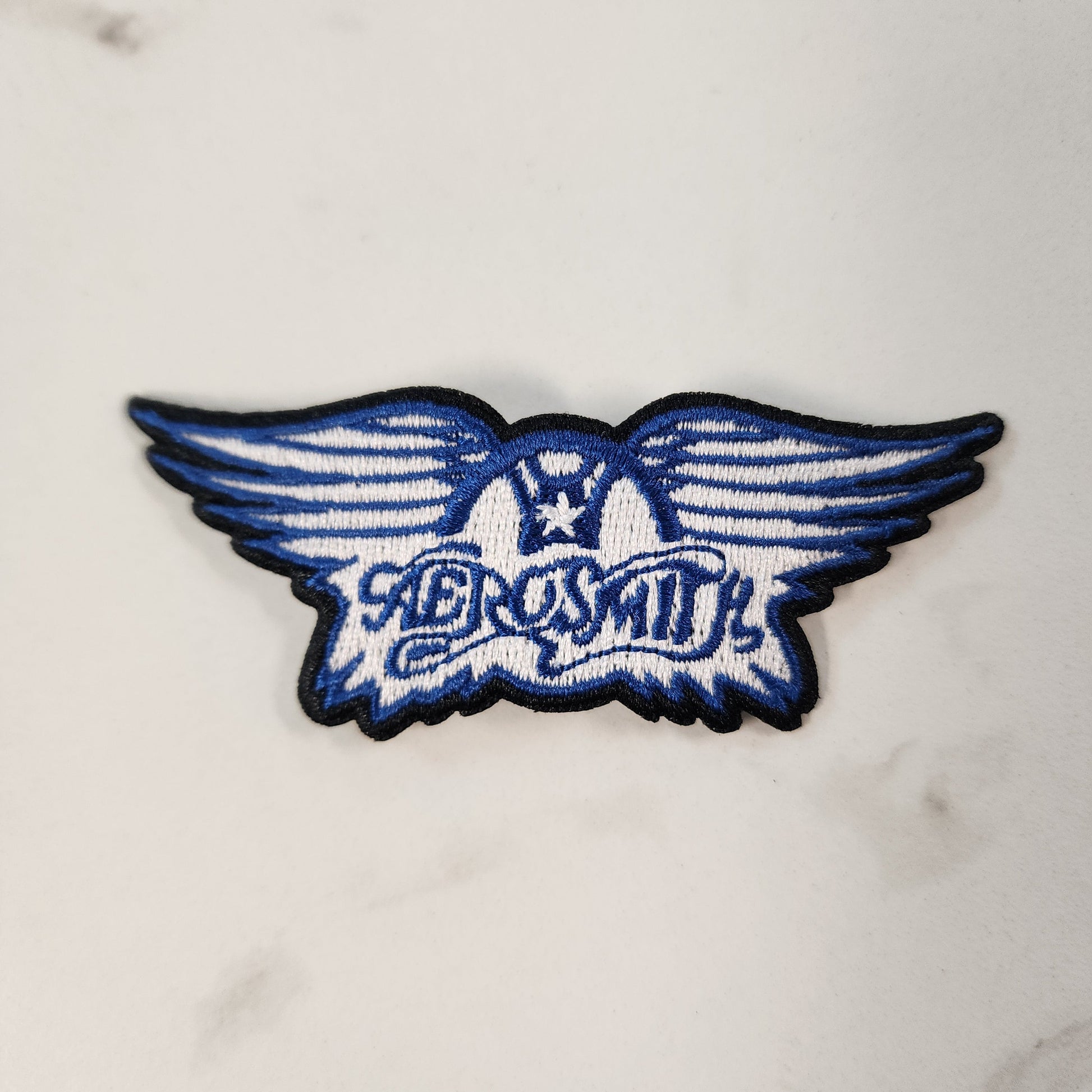 Blue and white winged logo patch on a marble surface